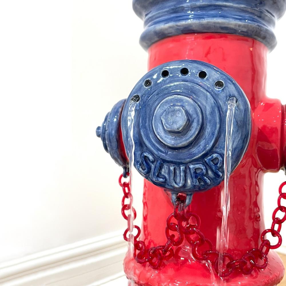 Closeup of ceramic fire hydrant sculpture with streams of water and sculpted word SLURP