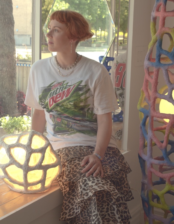 Portrait of the artist in a window nook surrounded by paper mache sculptures